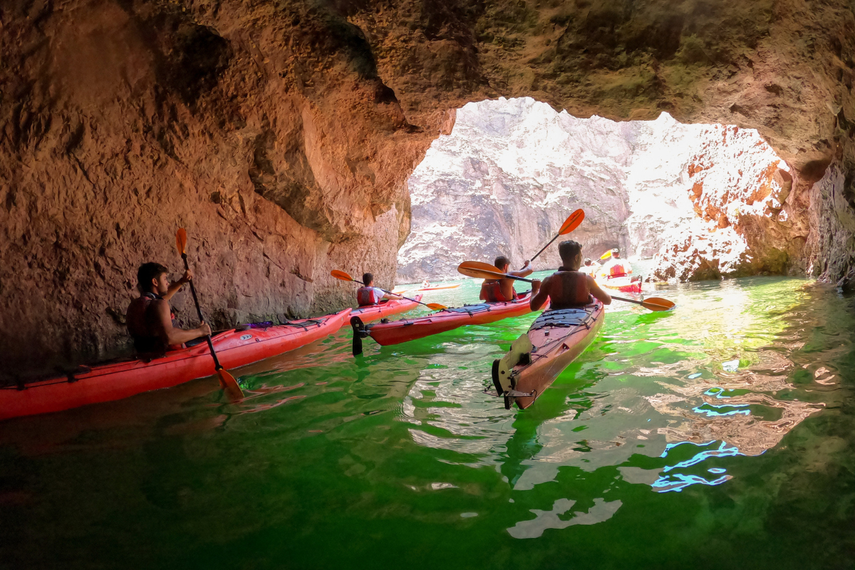 People kayaking in a cave with sunlight illuminating green water.
