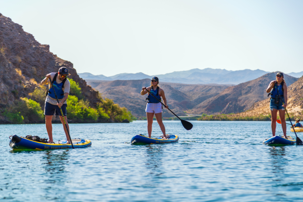 Three people paddleboarding on a calm river with rocky hills in the background.