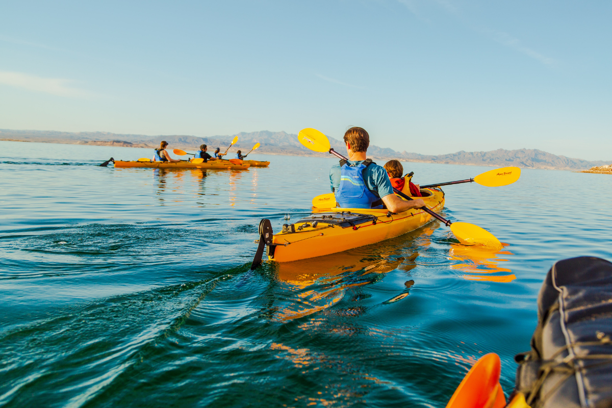 Two kayaks with people paddling on a calm lake with mountains in the background.