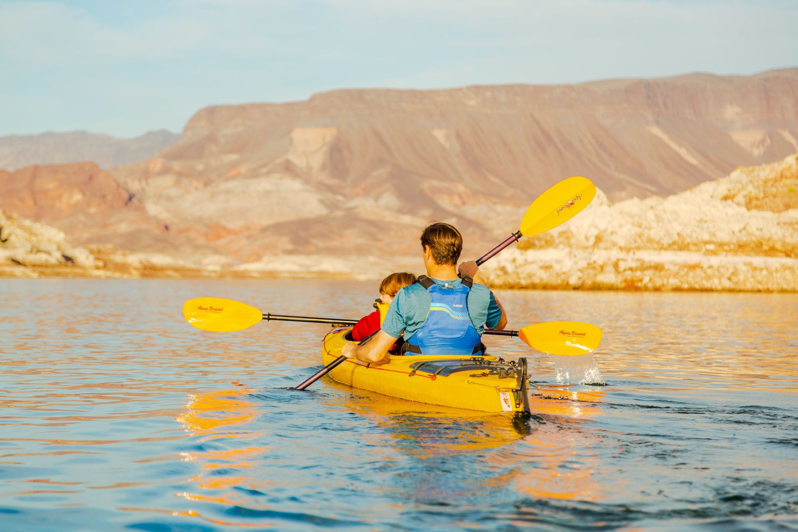 Two people kayaking in a yellow kayak on a lake with mountains in the background.