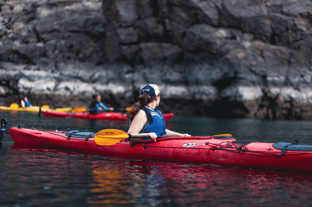 People kayaking on calm water near rocky cliffs.