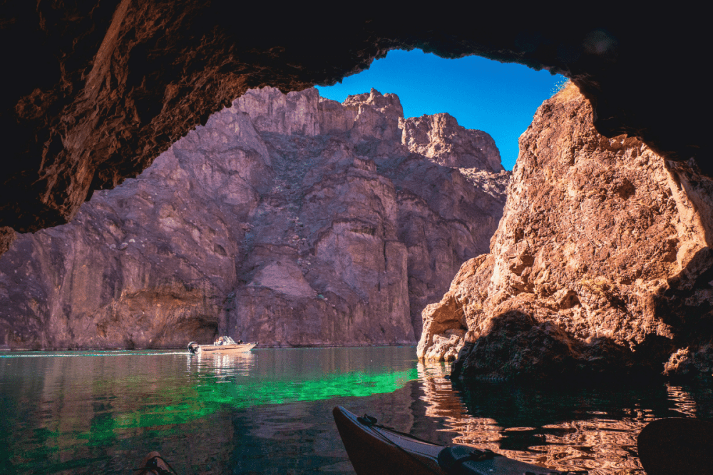 Cave opening view of a boat on a river with rocky cliffs and blue sky.