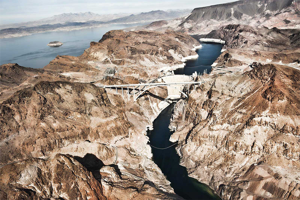 Aerial view of a dam and bridge in a desert landscape with river.