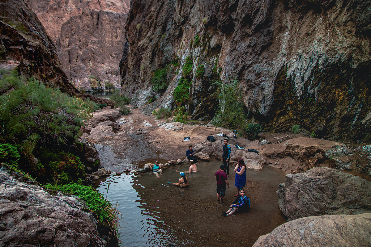 People relaxing in a small pool surrounded by rocky canyon walls.