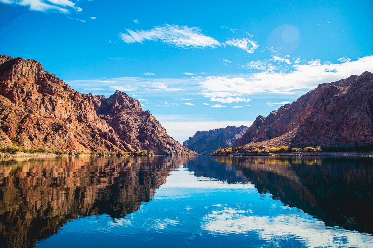 Mountain landscape with calm river reflection under clear blue sky.