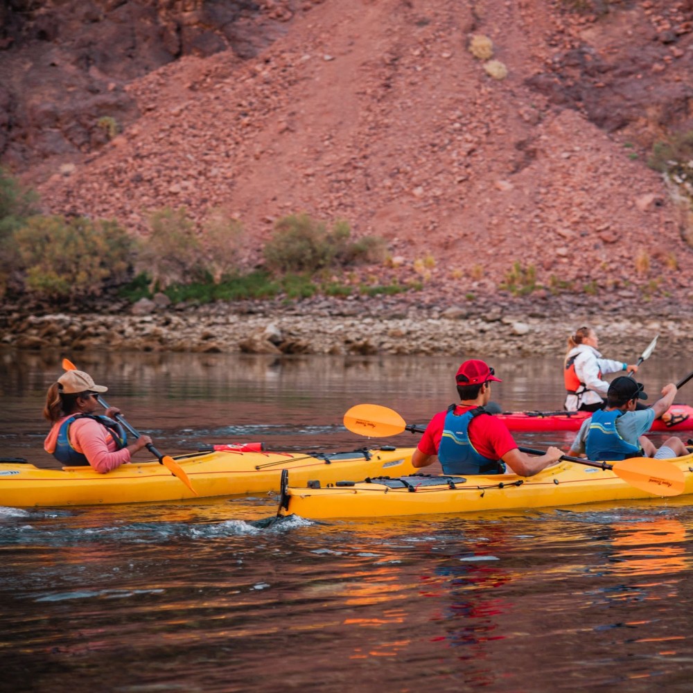 People kayaking on a river with rocky hills in the background.
