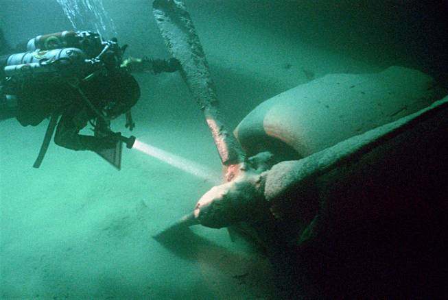 Diver exploring underwater plane wreckage with flashlight.