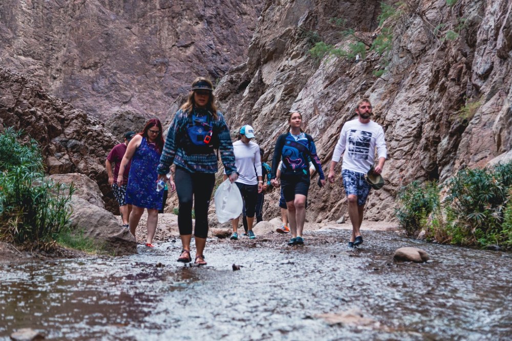 Group of people hiking through a rocky canyon streambed.