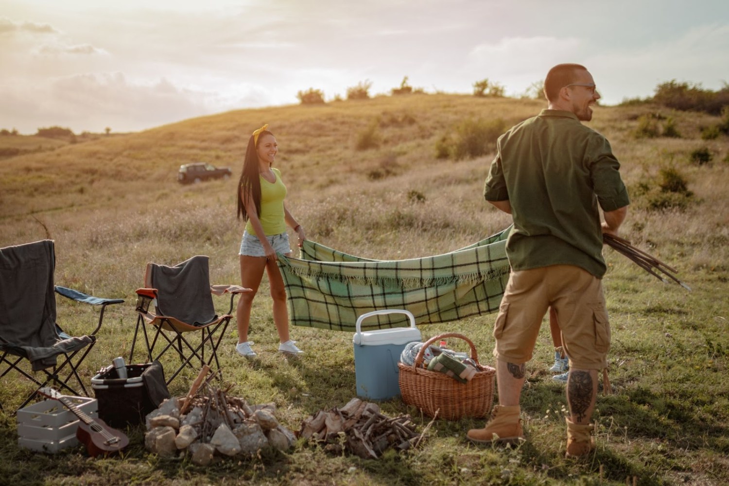 Two people setting up a picnic in a grassy field with chairs and supplies.