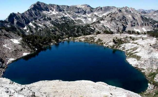 Mountain lake with clear blue water surrounded by rocky hills and patches of snow.
