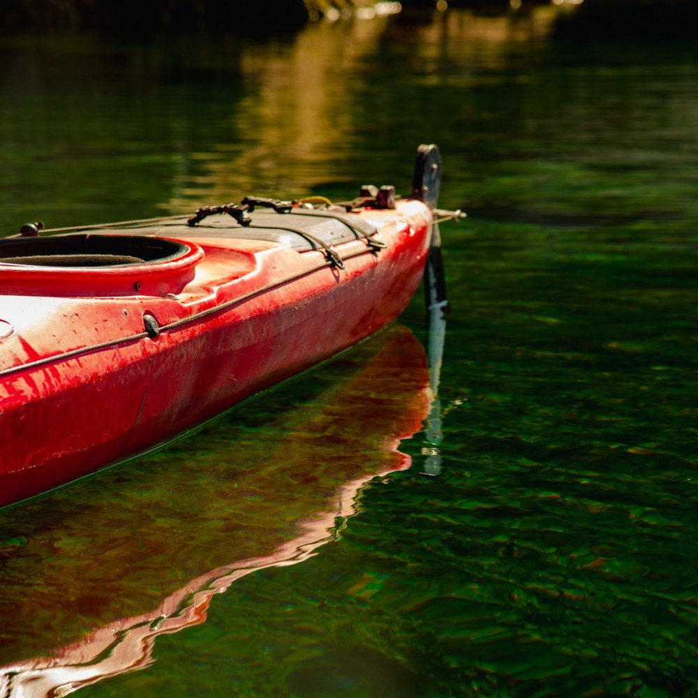Red kayak floating on clear green water with sunlight reflections.