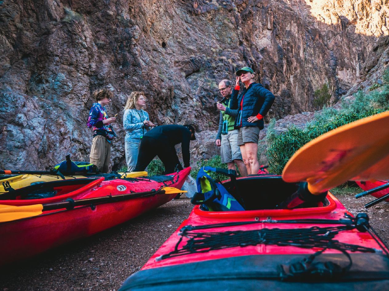 Group of people standing by red kayaks near rocky cliffs in outdoor setting.