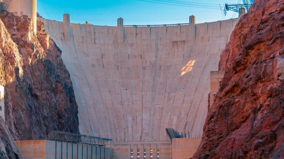 Large dam between rocky cliffs under a clear blue sky.