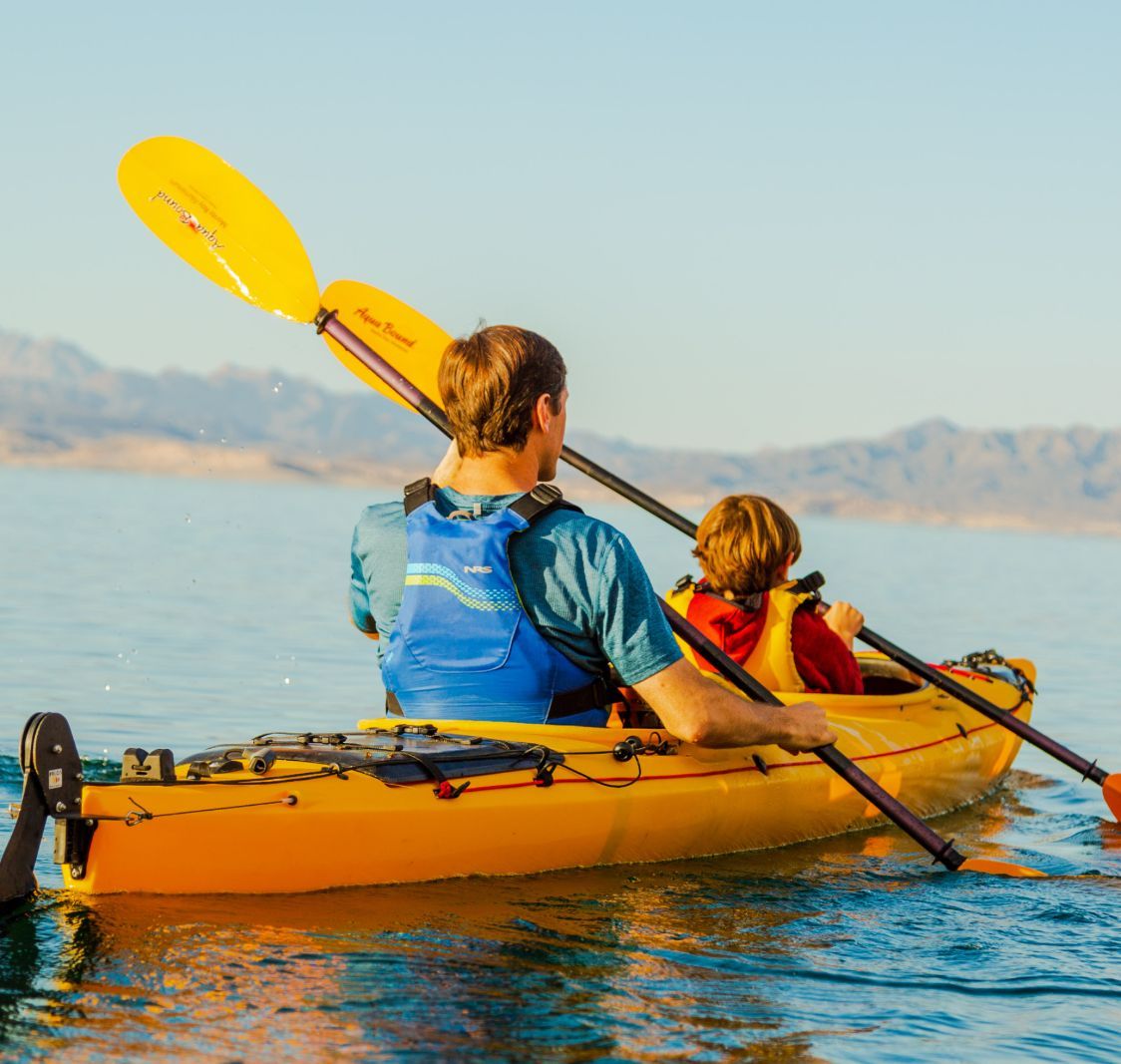 Two people kayaking on a lake with mountains in the background.
