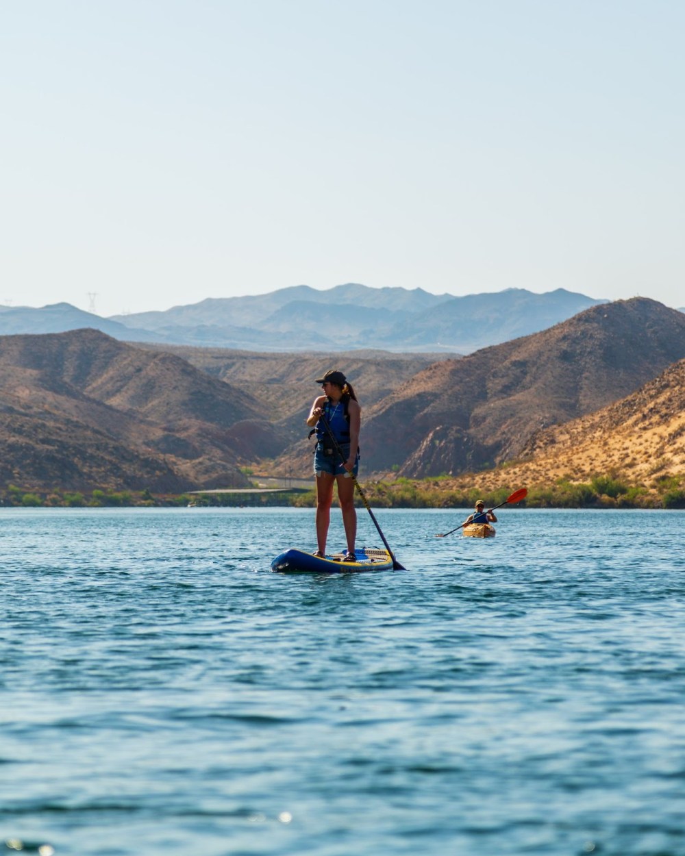 Person paddleboarding on a lake with mountains in the background on a sunny day.