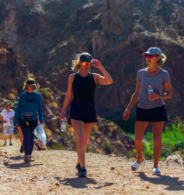 Four people hiking on a rocky trail with dry mountains in the background.