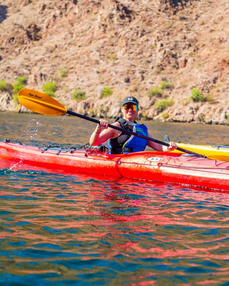Person kayaking on a lake with rocky hills in the background.