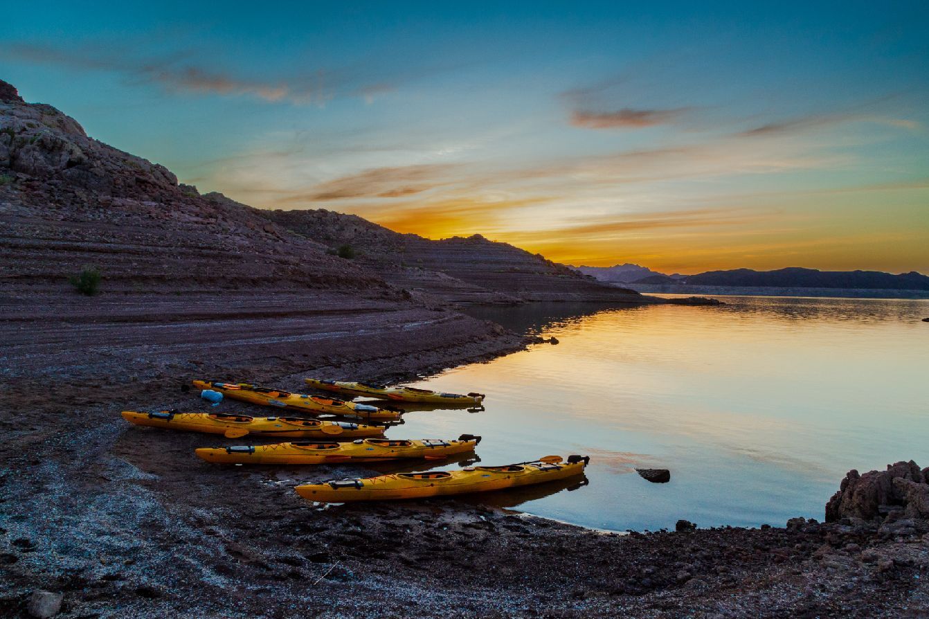 Yellow kayaks on a rocky shore at sunset near a calm lake.