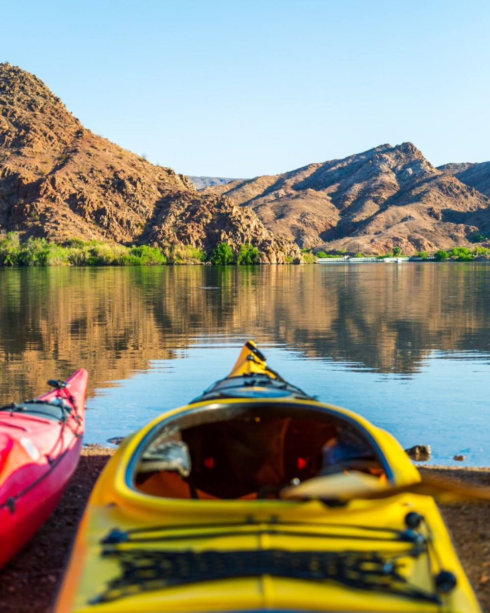 Red and yellow kayaks on lake shore with rocky hills in background.