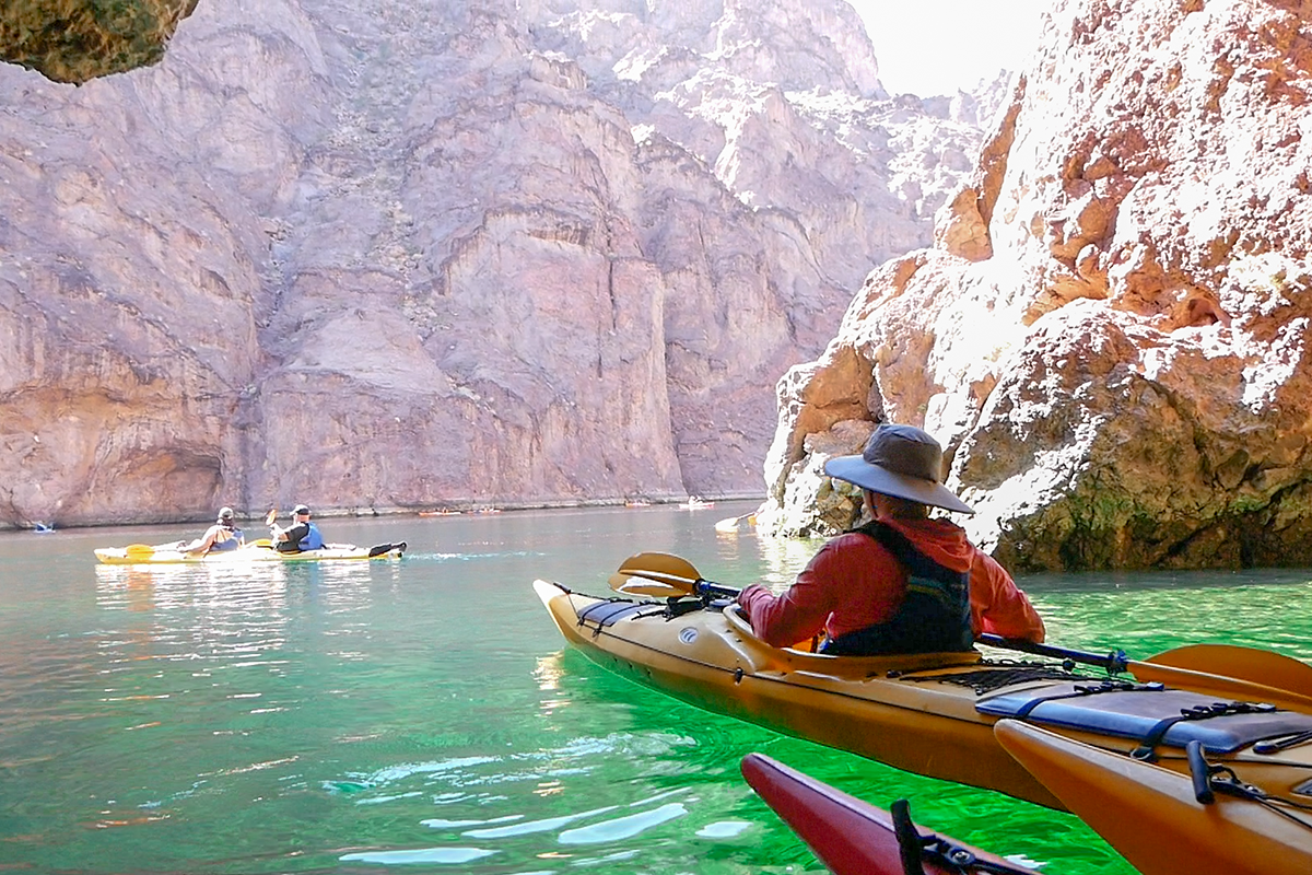 People kayaking on green water surrounded by rocky cliffs.