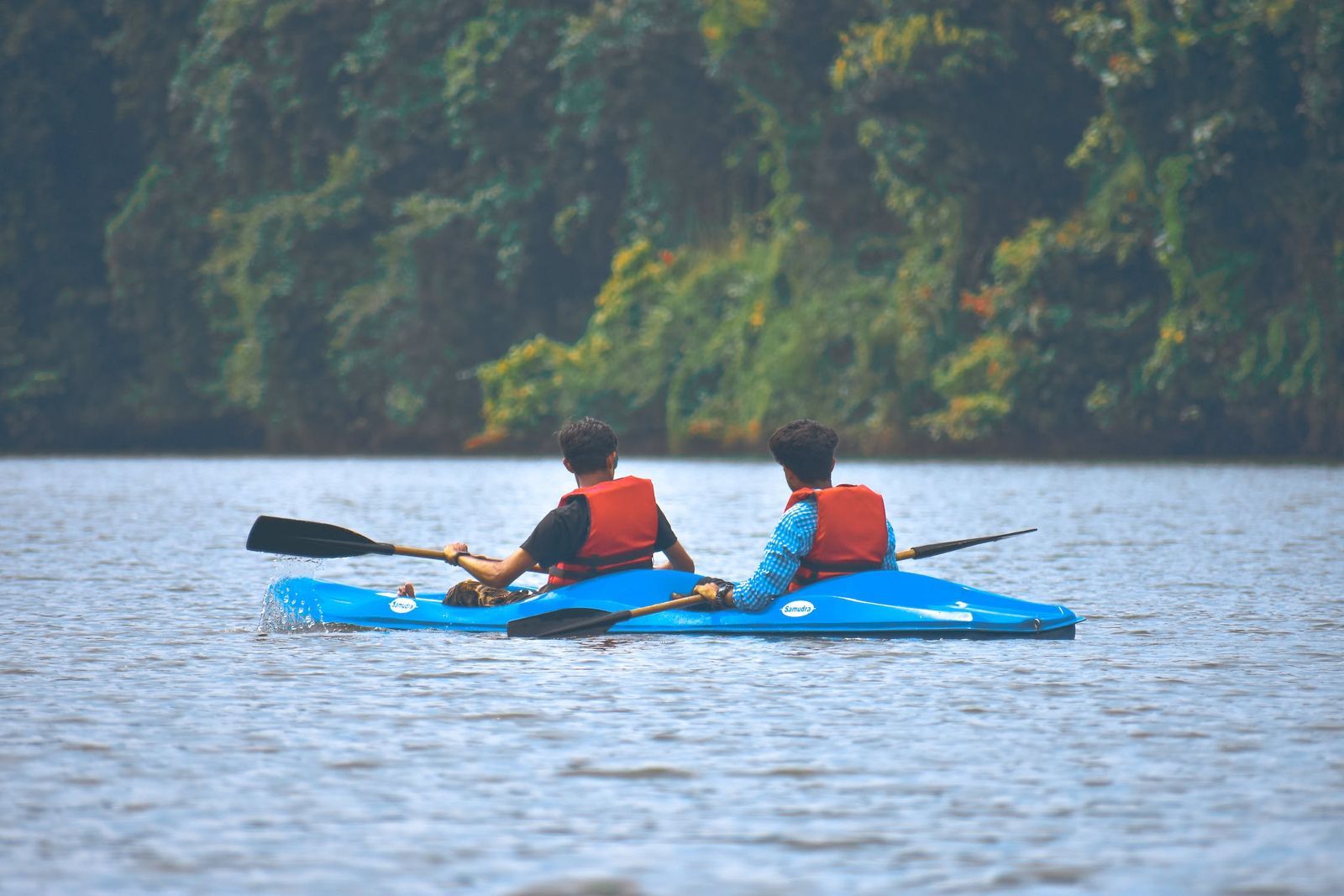 Two people kayaking on a calm river with lush greenery in the background.