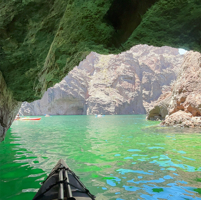Kayak entering a cave on a clear green lake with rocky cliffs in the background.