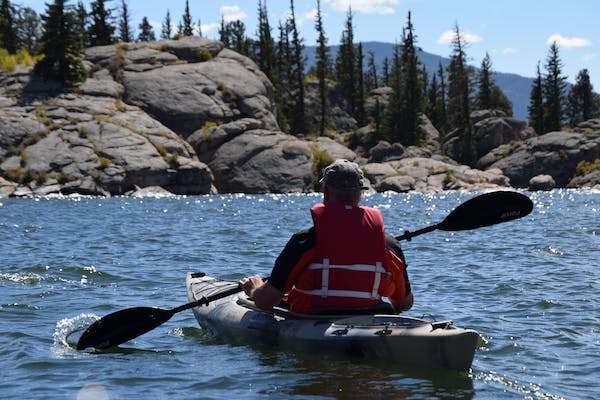 Person kayaking on a lake surrounded by rocks and trees on a sunny day.