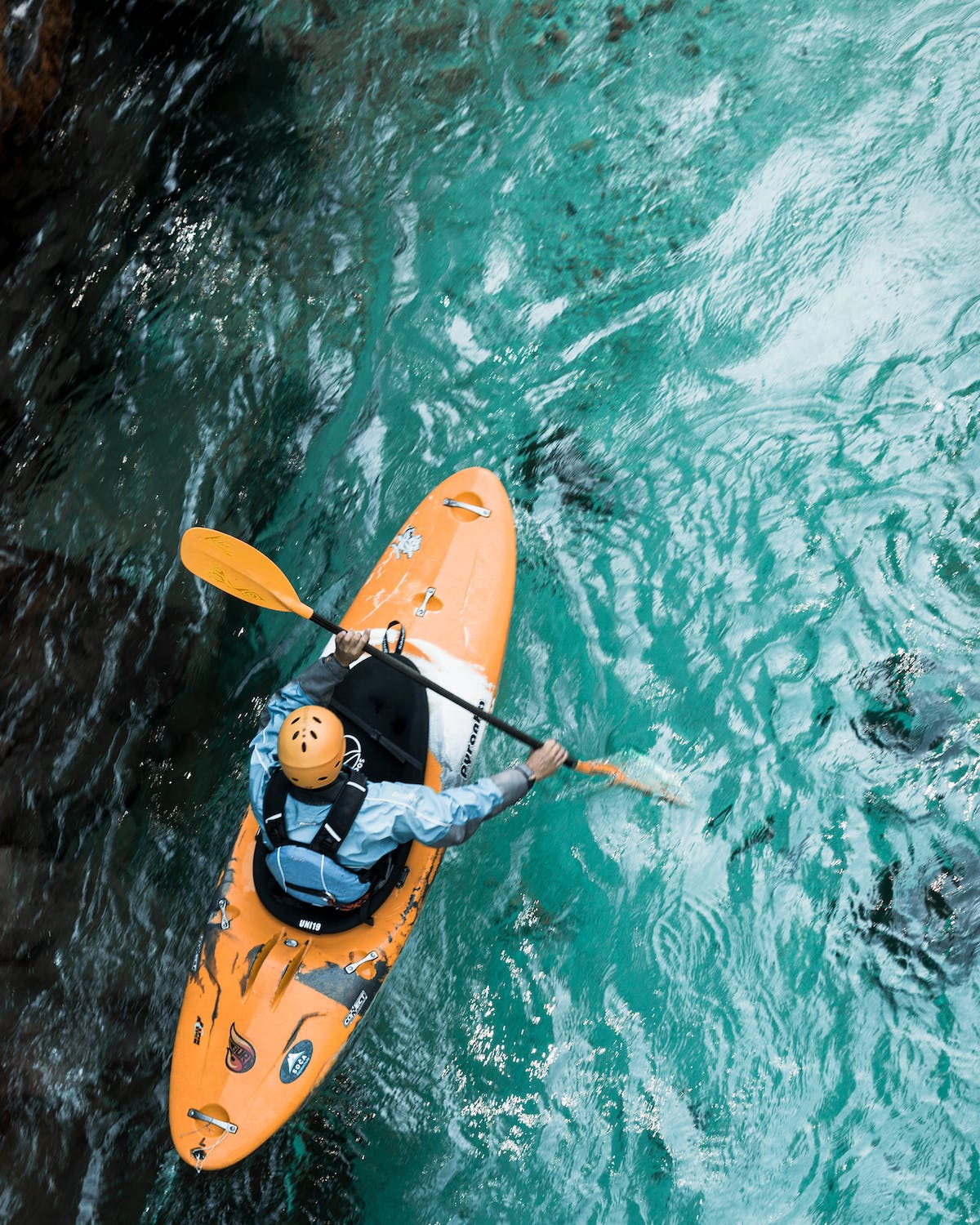 Person in orange kayak paddling on clear blue water, top view.