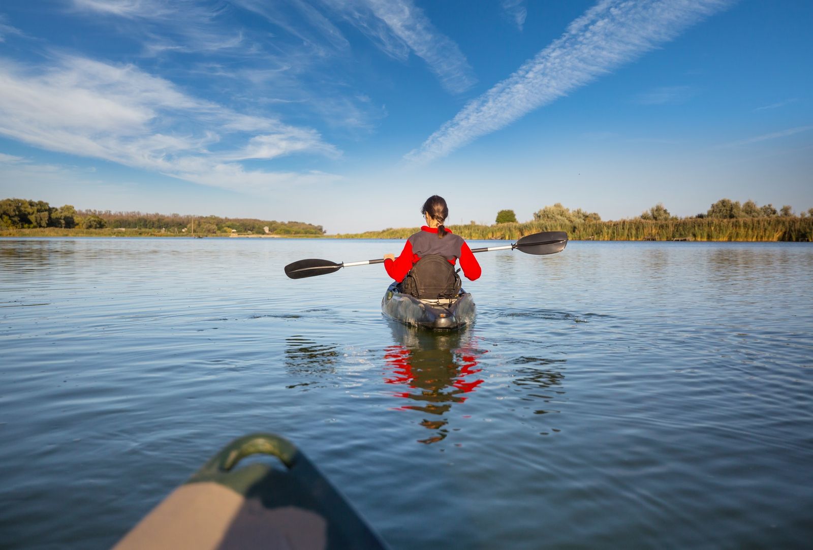 Person kayaking on a calm lake with clear blue sky and distant trees.