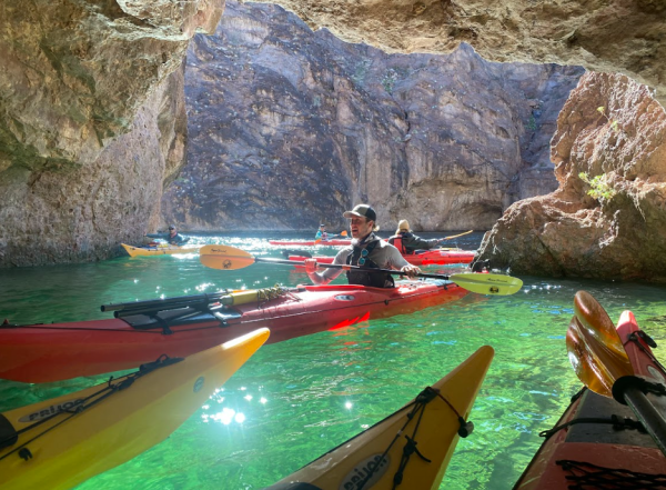 Kayakers in a rocky cave with sunlight reflecting on clear green water.