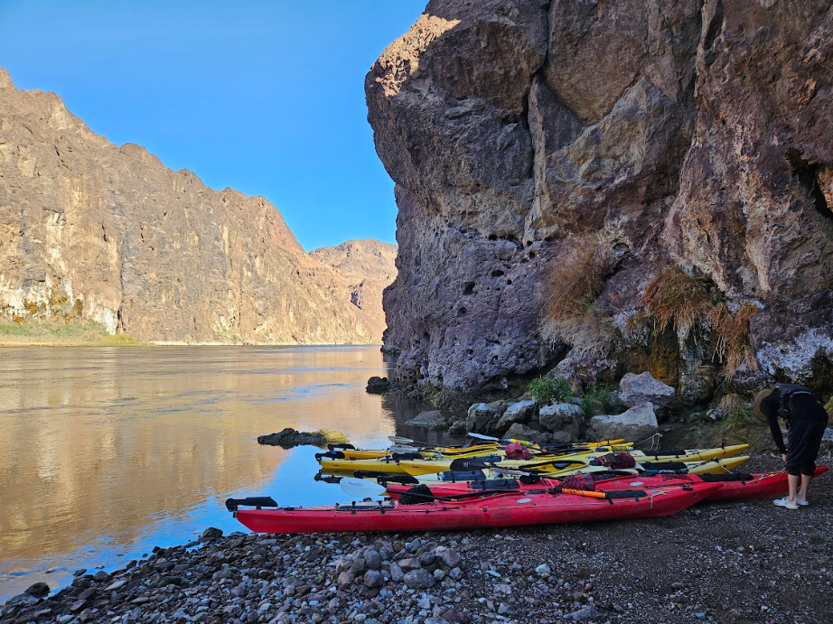 Kayaks on a rocky shore beside a river with canyon cliffs in the background.