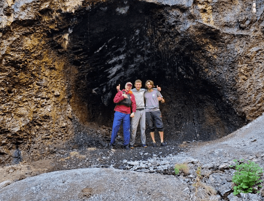 Three people standing in a rocky cave entrance, smiling and posing for a photo.