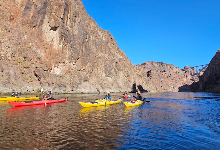 Kayakers paddle near rocky cliffs under a clear blue sky.
