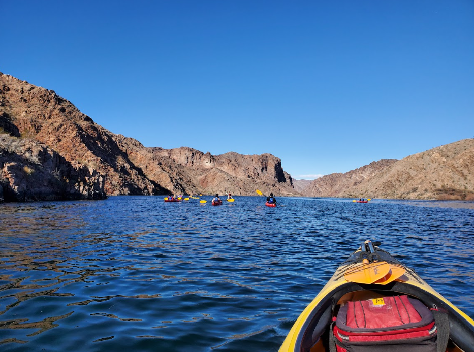 Kayakers paddling on a lake surrounded by rocky hills under a clear blue sky.