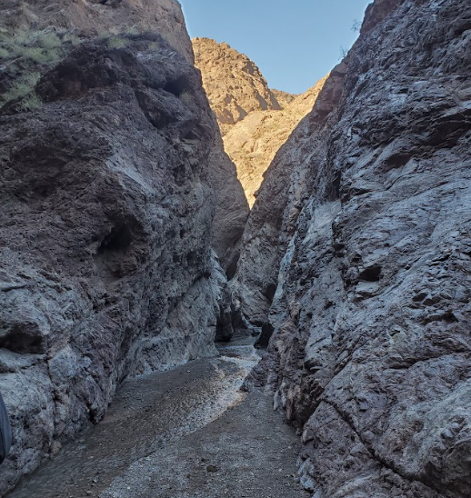 Narrow rock canyon with a gravel path and blue sky above.