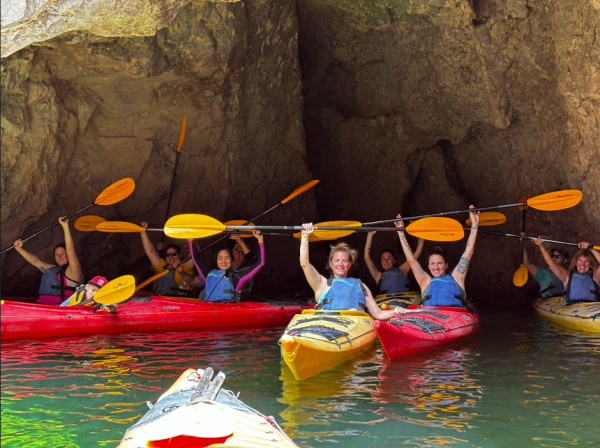 Group of kayakers raising paddles in a cave on clear water.