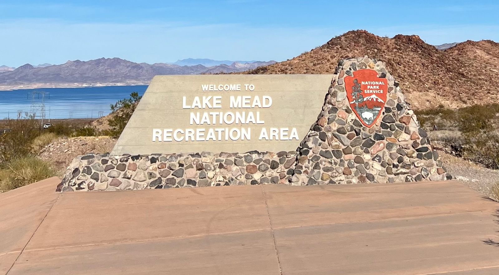 Stone sign for Lake Mead National Recreation Area with mountains and lake in background.