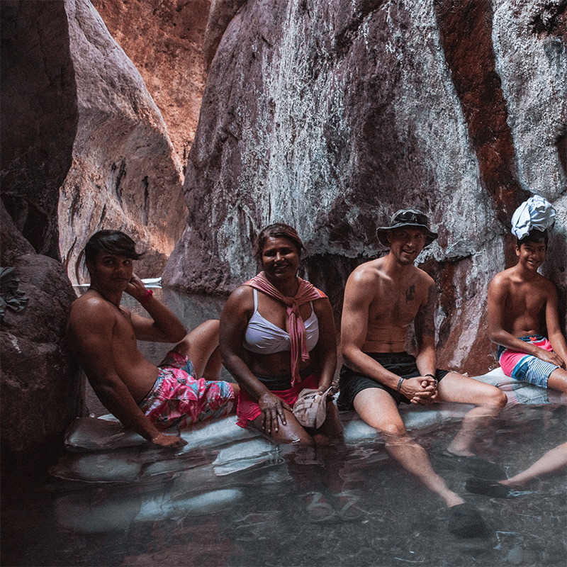 Four people sitting in a shallow rock pool inside a canyon.