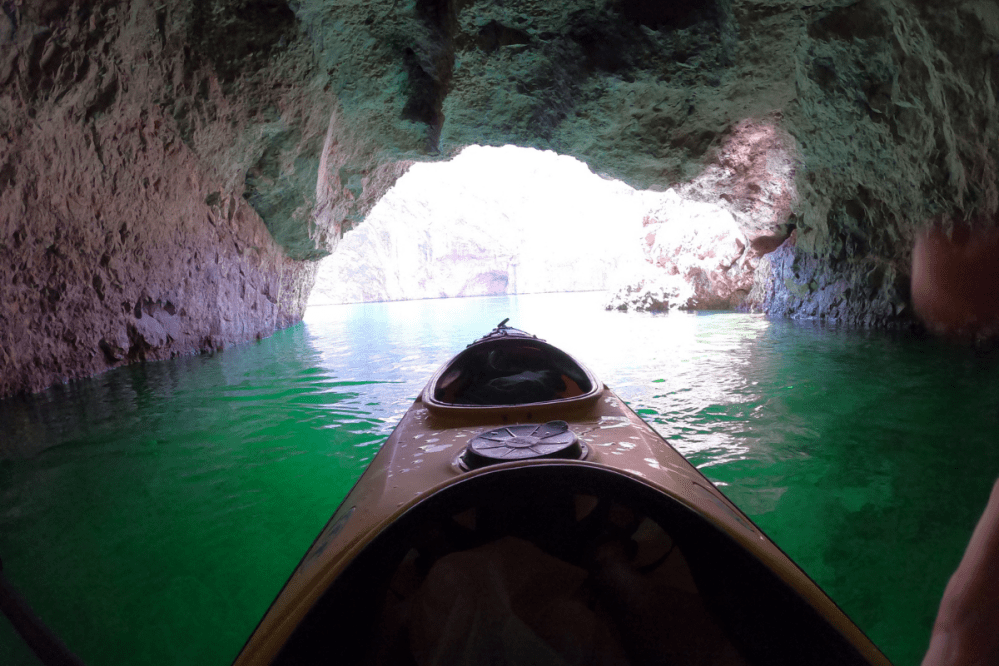 Kayak entering a cave with green water and rocky walls.