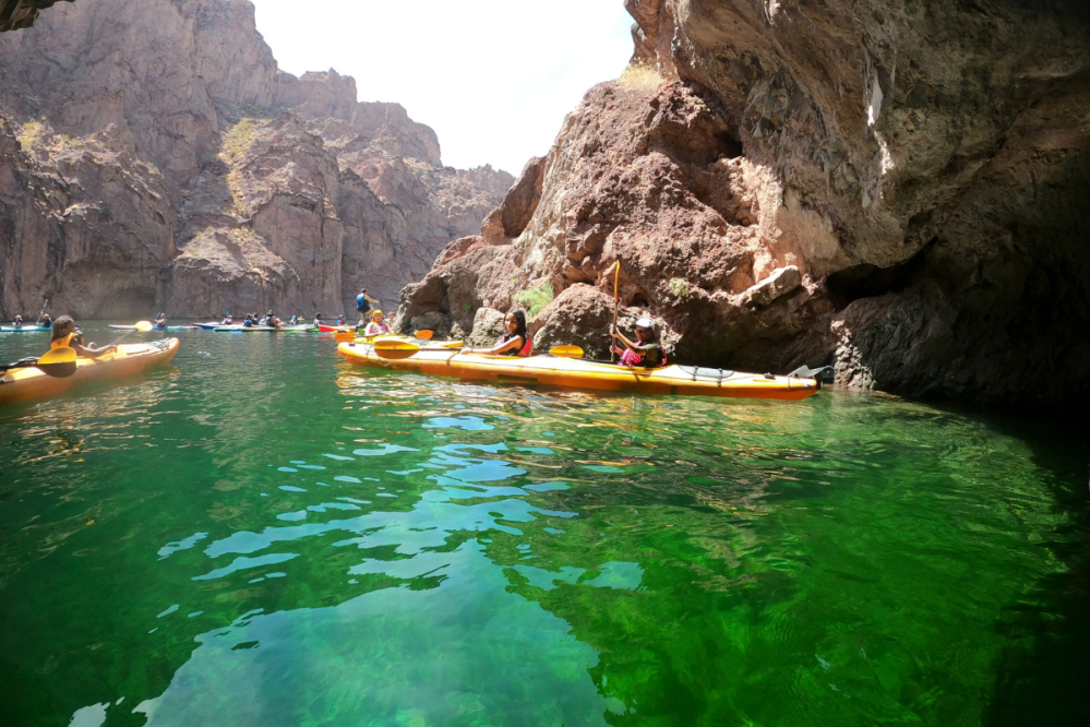 People kayaking on a green river surrounded by rocky cliffs.