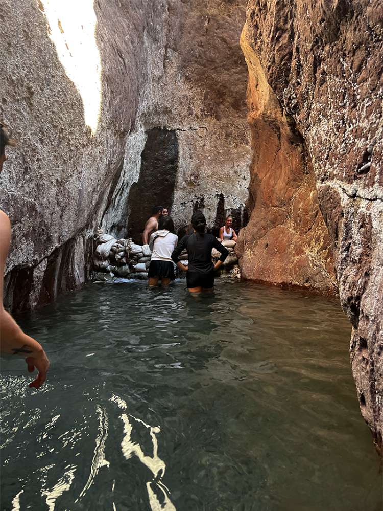 People wading through narrow canyon with sunlight illuminating rock walls and water surface.