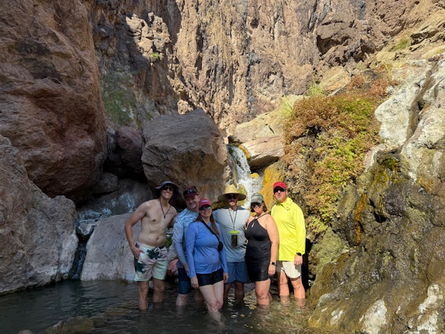 Group of six people standing in a rocky canyon pool with waterfall.