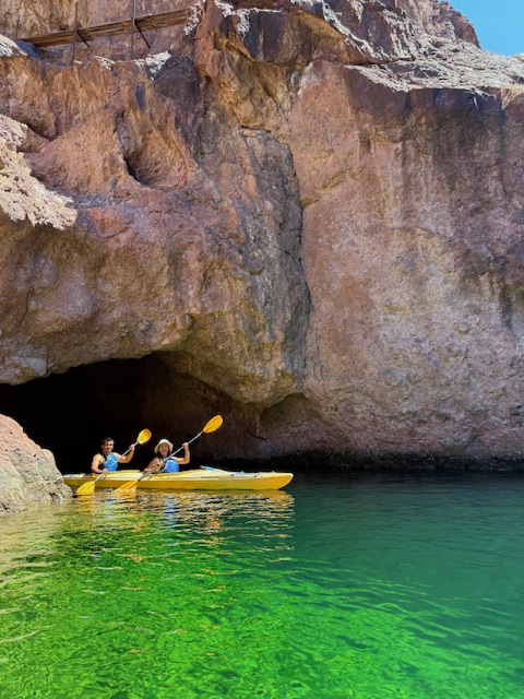 Two people kayaking in green water near a rocky cave entrance.