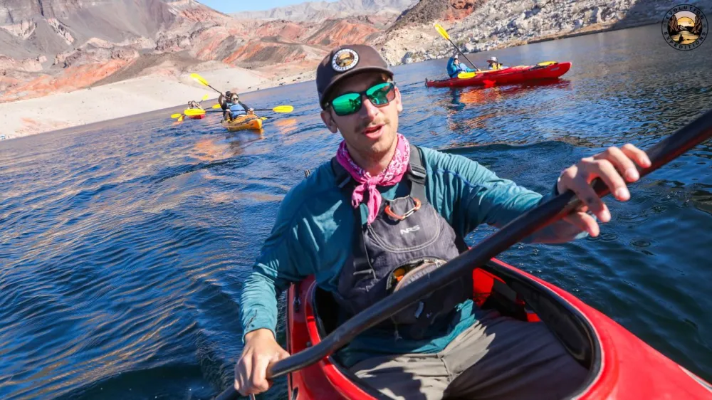 Person kayaking on a lake with mountains in the background under a clear sky.