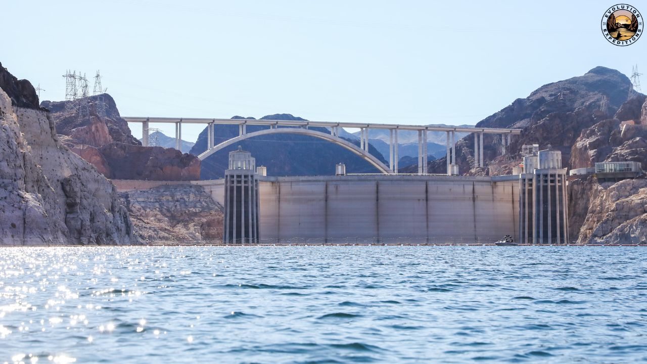 A dam and bridge over a calm body of water with rocky cliffs on either side.