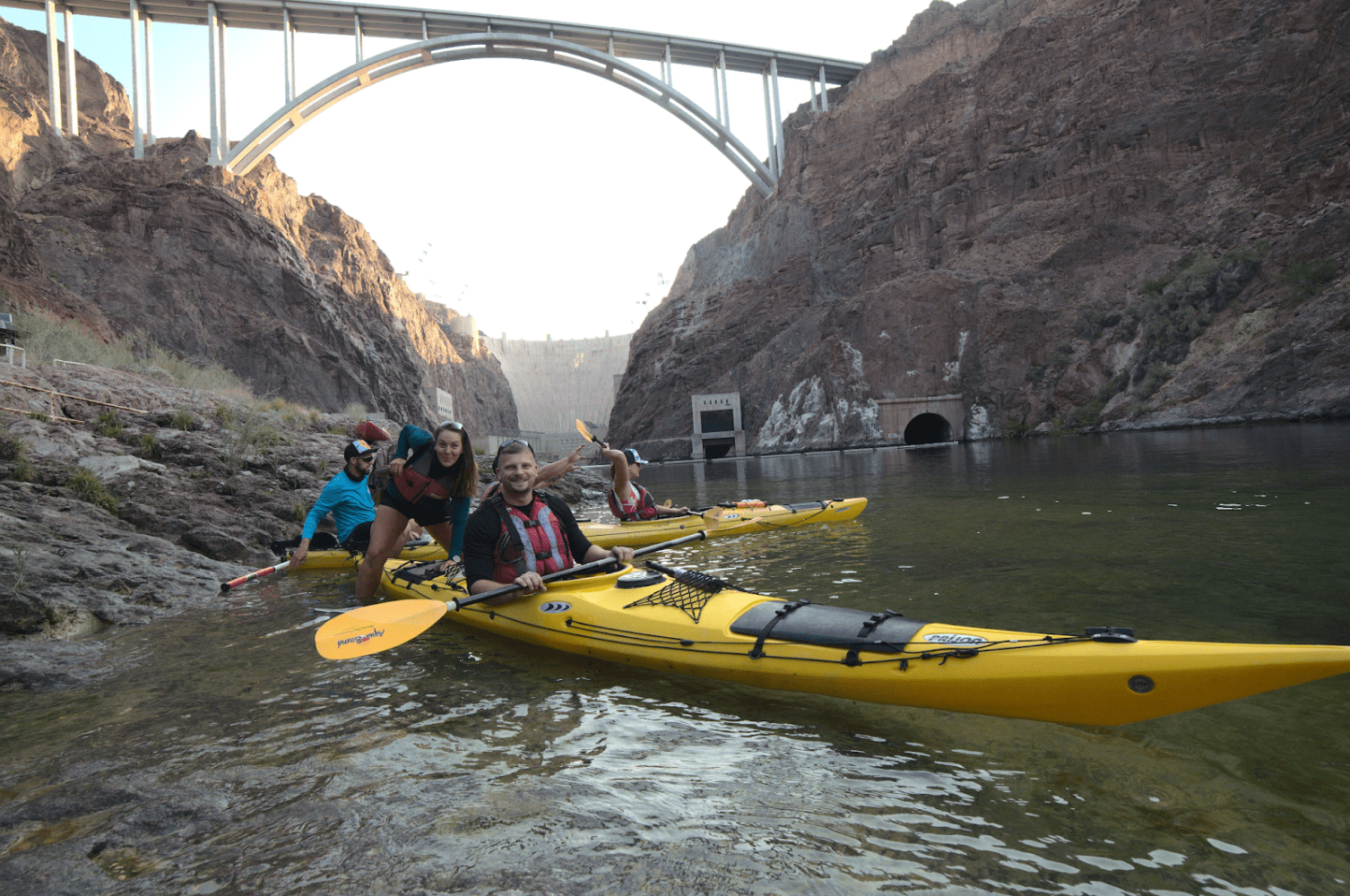 Group kayaking under a bridge in a rocky canyon area.