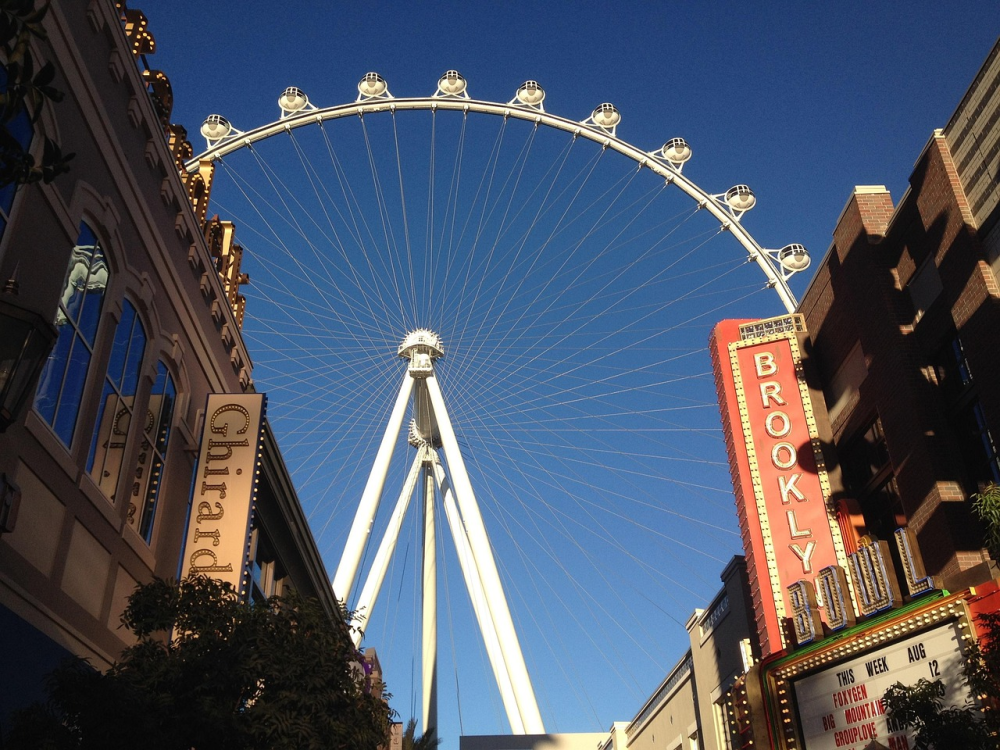 Ferris wheel between two buildings with theater signs under a clear blue sky.