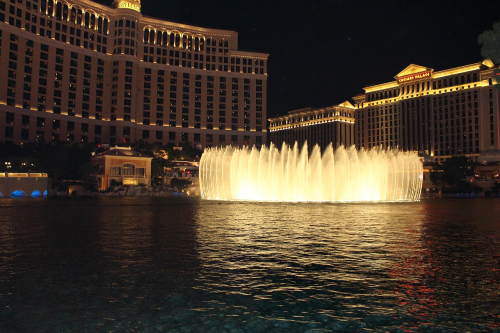 Night view of illuminated fountains with tall buildings in the background.
