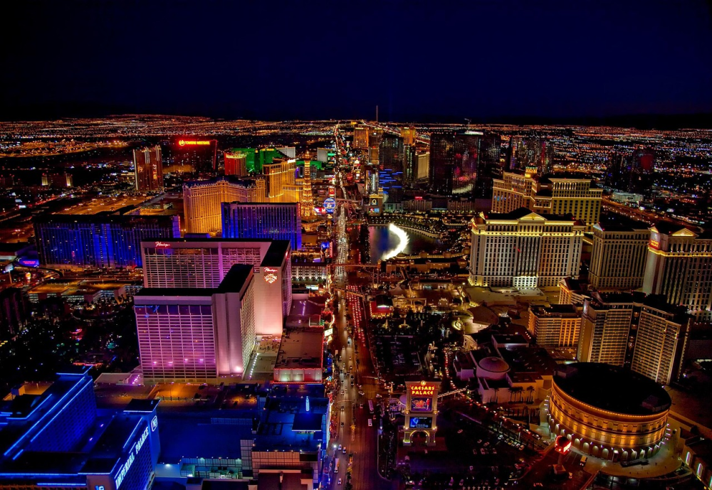 Aerial view of brightly lit cityscape at night, featuring colorful buildings and illuminated streets.