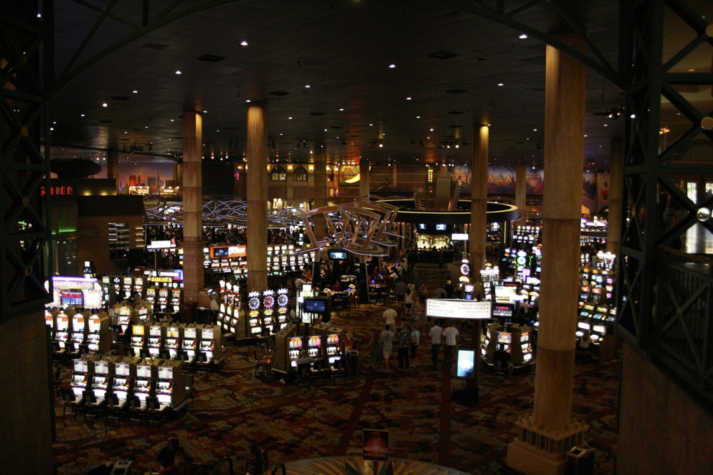 Interior of a casino with slot machines and people walking around.
